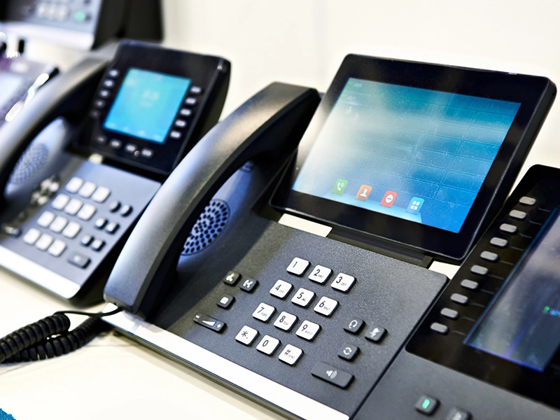 A modern office team using VoIP phones, headsets, laptops, and business communication tools.